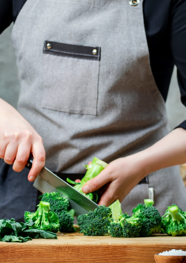A person in an apron cutting broccoli florets